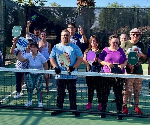 a group of individuals with pickleball paddles standing behind a tennis net