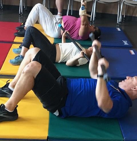 3 people laying on their backs on colorful mats pushing weighted bars